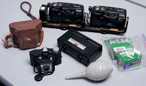 手前左が一光社から1950年に発売されたスタート35。中学生の中島さんがアルバイトでためた金で購入した初めてのカメラだ。後ろはリコーのコンパクトカメラ、マイポートで作製したステレオカメラ。それにフィルムと電池、ブロアーは三種の神器と呼んでいつも持ち歩いている。中央は、ポジフィルム2枚を入れて迫力ある立体画像が楽しめる専用のビューアー