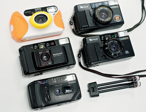 石井さん所有の「駄カメラ」たち。右上から時計回りに、フジAUTO-8 QD TATE YOKO（阪神タイガース優勝記念モデル）、同・通常モデル。コニカ KANPAIと専用三脚。ナショナルC-D600AF。コニカMERMAID