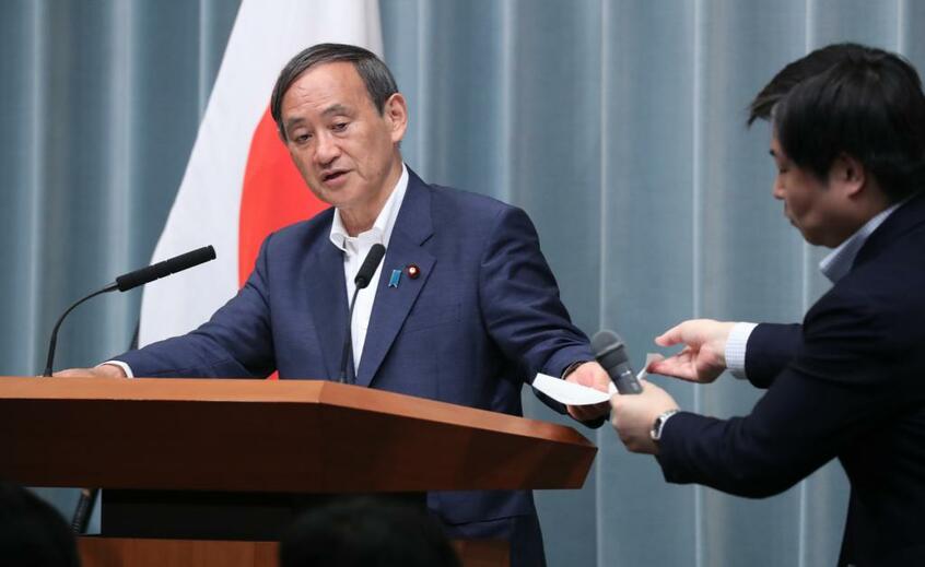 記者会見で、上村秀紀報道室長(右)から資料を受け取りながら質問に答える菅義偉官房長官=2019年7月23日 (c)朝日新聞社