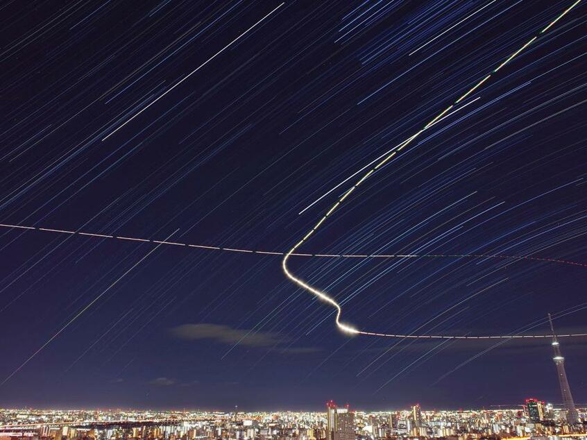 南千住の住宅街からは、東京スカイツリーを包み込むような星々が観測できた。流れる光は航空機の軌跡だ(撮影/佐々木勇太さん提供)
