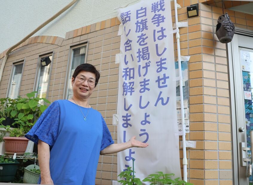 自宅1階で喫茶店を開く藤岡美千代さん。戦争に加担しない、戦争を許さない、という思いを込めて、店の前に「PTSDの日本兵家族会・寄り添う市民の会」がスローガンを掲げている=2025年7月15日、大阪市(photo 大久保真紀)
