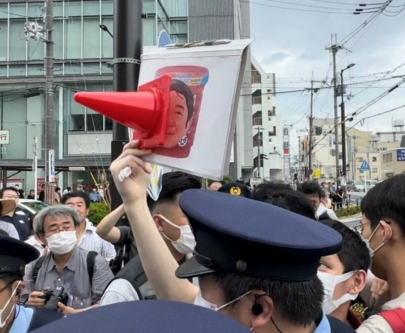 安倍元首相とみられるイラストが描かれたプラカードを掲げる男性