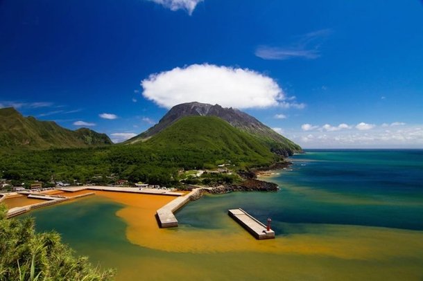 頭に雲を抱く硫黄岳。島周辺の海は硫黄岳からの成分により褐色に染まっている。（写真提供：三島村役場）