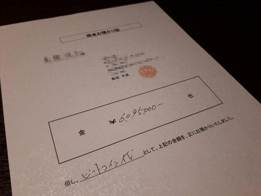 東京都内の女性が柴田容疑者に６０９万５千円を手渡しした際に受け取った「現金お預かり証」。「ビットコイン代として」と書かれている　（ｃ）朝日新聞社