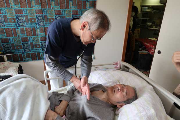 脳出血で療養中のヨウコさんの夫の胸に聴診器をあてる宮崎さん