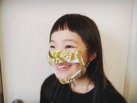 口を覆う部分が透明になった「シースルー愛マスク」。「マウスシールド」等の名称で上部が開放された透明マスクが出回っているが、このマスクは顔に密着するため安心感があると人気を博す。写真提供：上中まや）