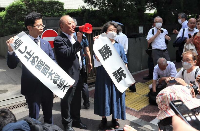 （４）東京高裁判決後、「勝訴」と書かれた紙を掲げる山本志都弁護士、「差し止め範囲大幅拡大」と掲げる中井健人弁護士と、ハンドマイクを持って説明する西島藤彦・部落解放同盟委員長＝２０２３年６月２８日、東京・霞が関、北野隆一撮影