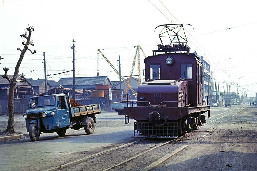 国鉄若松駅に続く電車道の路上には、昼休みで無人の市電（電気機関車）がポツンと佇んでいた。その横をよれよれのダイハツ三輪トラックが走り抜けていった。中川通七丁目（撮影／諸河久：1968年3月15日）