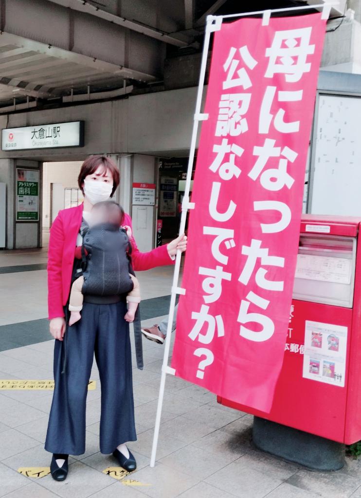 抗議ののぼりを掲げて、子どもを抱えながら街頭に立つ大野氏（本人提供）