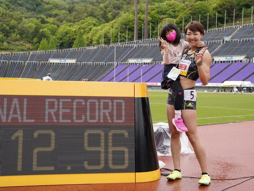 今年4月、女子100メートル障害を日本新記録で優勝した寺田明日香選手。長女の果緒ちゃんを抱いて記録の横に並んだ (c)朝日新聞社