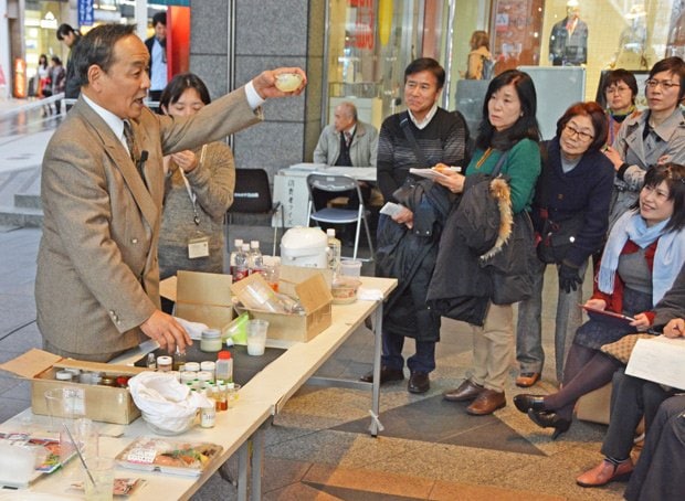 食品添加物を混ぜて「かつおだし」をつくり、味覚を壊す「黄金トリオ」を説明する安部さん（左）＝２０１６年、熊本市内で（ｃ）朝日新聞社
