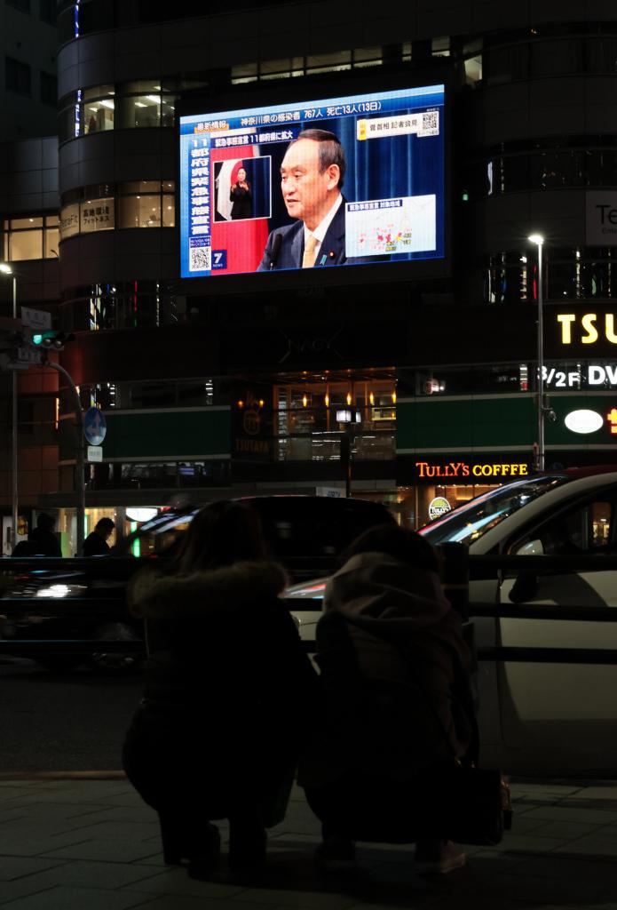 愛知県などへの緊急事態宣言について会見する菅義偉首相を映す大型ビジョンを、若者が見つめていた／1月13日、名古屋市のJR名古屋駅前　（ｃ）朝日新聞社