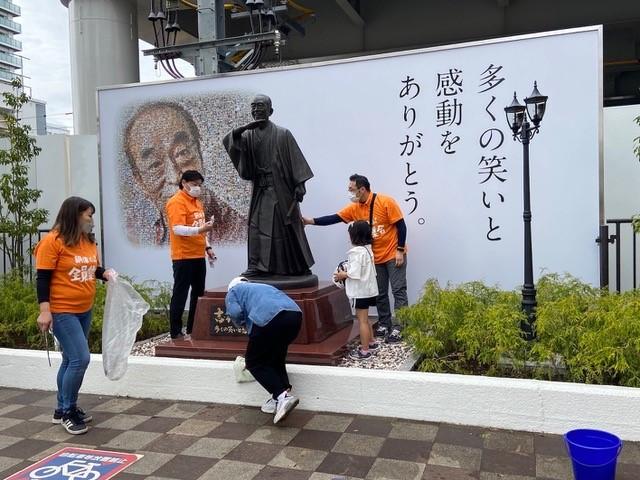 東村山駅前の志村けんさんの銅像周辺を掃除する「志村けんさん銅像プロジェクト実行委員会」メンバーら＝３月２７日、高鍬真之撮影