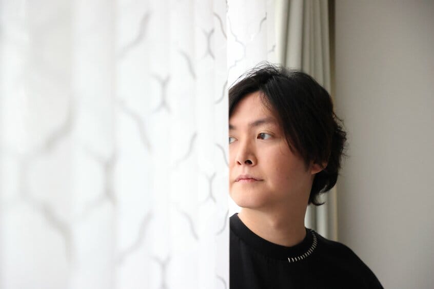 カーテン越しに格好よく(本人ではなくAERAの希望アングル)。実は事務所がそこそこ散らかっていて背景がシンプルな場所が少なかった(撮影:松永卓也/写真映像部)