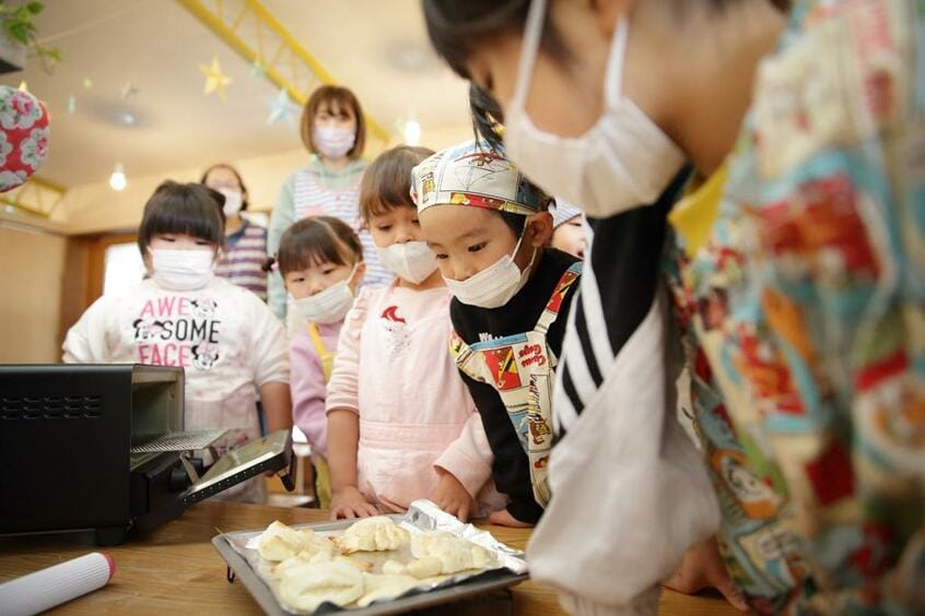カミヤト凸凹保育園+plus/「日々のパン」による親子パン教室(左)。教室は開け放たれて半屋外の回廊とつながっている。日の当たる回廊に机を出してお昼を食べる子どもたち(photo 小暮誠)