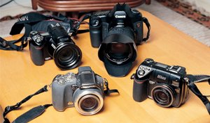 前列左のオリンパスSP-550UZは、35ミリフィルム換算で28～504ミリと18倍ズームで手ブレ補正がついているので海外での調査撮影に最適だという。コンパクトデジカメはニコンクールピクスの描写がお気に入りで、8400（前列右）と8800VR（後列左）は、それぞれ広角用、望遠用とレンズ交換でなく、カメラ交換で使い分けている。EOS5Dは描写はいいのだが、重いのが難点だという