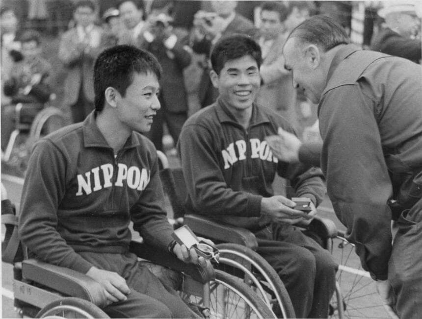 １９６４年のパラリンピック東京大会。卓球の男子ダブルスで優勝し、日本唯一となる金メダルを大会役員から渡される、渡部藤男選手（右）と猪狩靖典選手　（ｃ）朝日新聞社