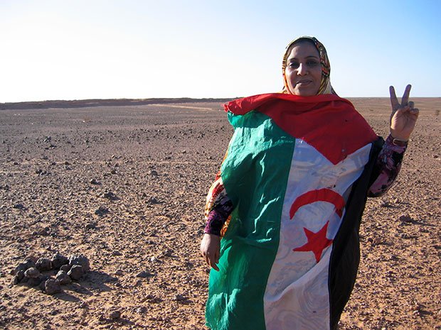 西サハラ亡命政府「サハラ・アラブ民主共和国」の国旗をまとう女性。背後に「砂の壁」が見える。これ以上近づくと地雷とモロッコ軍の銃撃という危険がある（撮影／川名生十）