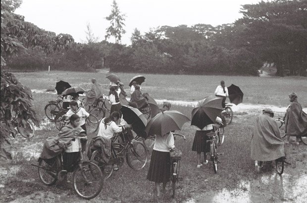 突然の雨。慌てて雨かっぱをかぶったり、傘を差したりして、自転車にまたがり、家路を急ぐ女子学生たち。沖縄本島北部にあった県立第三女学校(通称・三高女、現・名護高校)の生徒と思われる (C)朝日新聞社