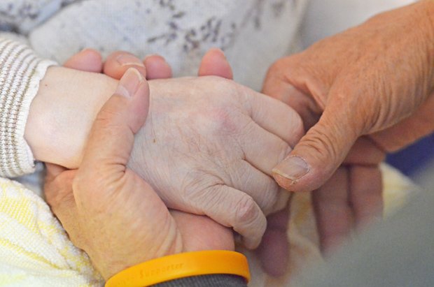 老人医療施設で暮らす認知症の妻の手を握りながら、介護をする男性（写真は本文と関係ありません）（ｃ）朝日新聞社