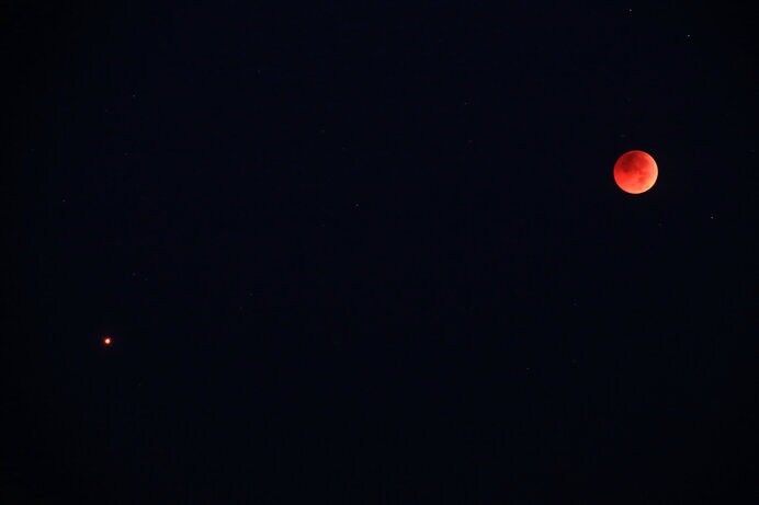 赤銅色の月食の月よりも赤く輝く火星(左)は、きわめて印象的です
