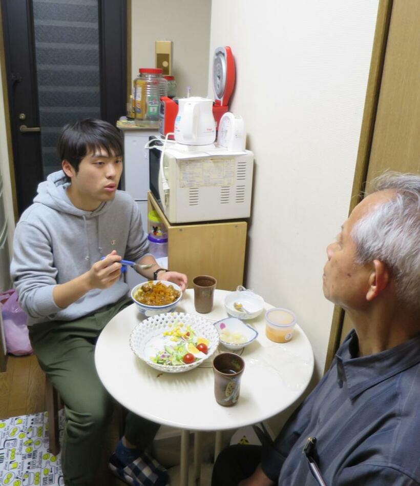 異世代ホームシェアで一緒に住む宮本幸一さん（手前）と大学１年生の高橋和さん。話しながら夕食を一緒に食べる