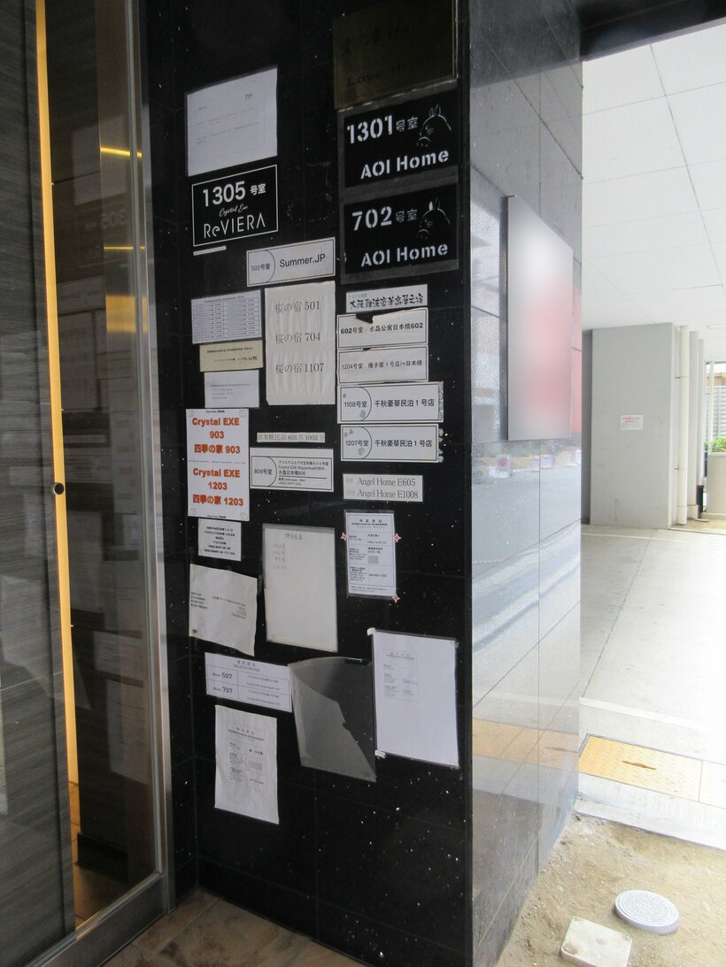 「民泊雑居マンション」。入り口にはさまざまな会社が運営する民泊の表示がある。「苦情窓口」には中国人とみられる名前が記されている＝松村嘉久教授提供