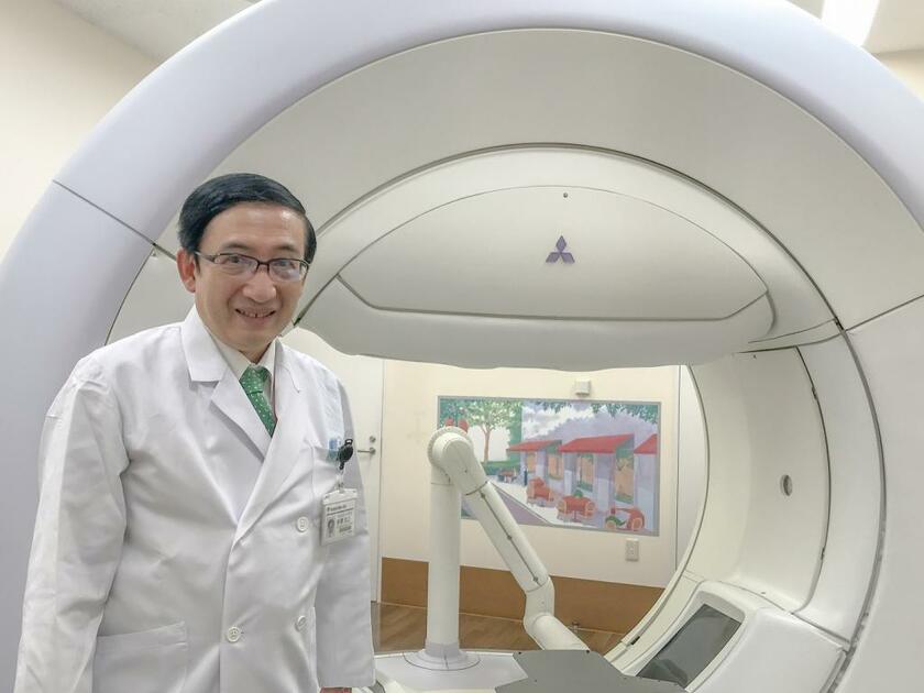 都立駒込病院放射線診療科治療部部長の唐澤克之医師。背景は放射線治療装置の「VERO-4DRT（ヴェロ）」（撮影／白石圭）