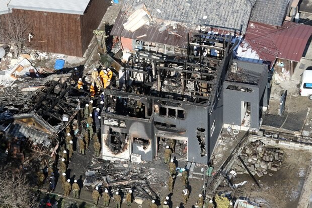 現場検証する自衛隊員ら。焼けた民家の近くにヘリの機体の一部が見える　（ｃ）朝日新聞社
<br />