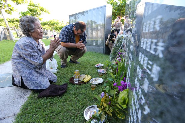 「慰霊の日」の朝、戦争犠牲者の名前が刻まれた「平和の礎」の前に座り込んで手を合わせる人たち。今年は新たに84人の名が加えられ、刻銘者は２４万１４１４人になった／６月２３日、沖縄県糸満市　（c）朝日新聞社