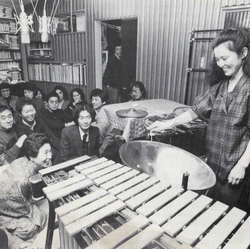 １９８４年９月、立花さん宅のスタジオで打楽器奏者の吉原すみれさん（右）が演奏。作家の澤地久枝さん（左前）、妹尾さん（澤地さんの後ろ左側）、立花さん（妹尾さんの右隣）、ミュージシャンの小室等さん（右奥の壁際）らが集まった。「“立花趣味”に付き合った豊かな良き時代でした」と蜷川さん（小室さんの左、座っている男性）　（写真提供／蜷川真夫さん）