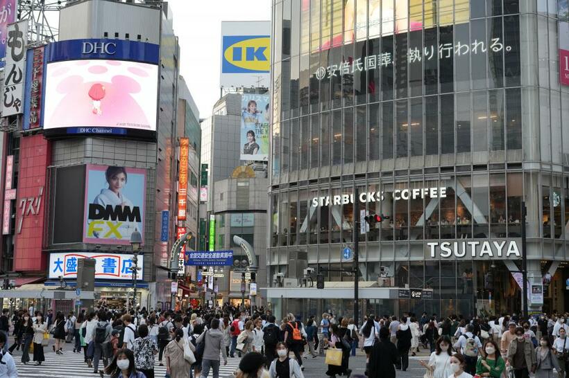 多くの人が行き交う渋谷のスクランブル交差点。「安倍氏国葬、執り行われる」のニュースを流す電光掲示板（奥）＝9月27日、東京都渋谷区