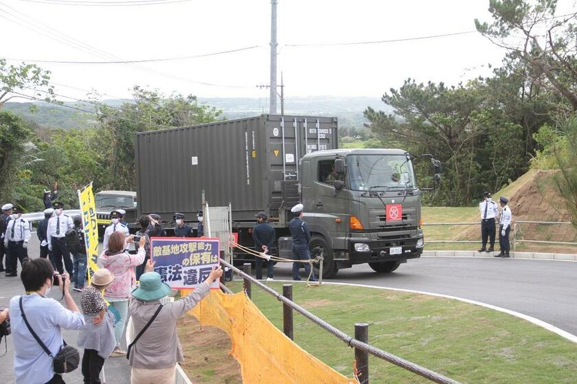 新設された陸上自衛隊石垣駐屯地に、ミサイルなどの弾薬を運ぶトラック。沿道には自衛隊配備に反対する住民の姿もあった＝３月18日（八重山毎日新聞提供）