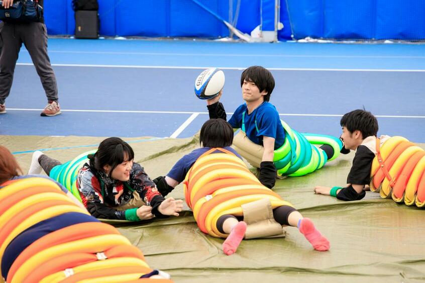 イモムシラグビー／カラフルなコスチュームを着て、ごろりと寝ころべば気分はイモムシ。ほふく前進したりゴロゴロ転がったりしながらラグビーボールをつなぐ。炎天下のグラウンドの上で「焼きイモムシ」にならないようにと、この日は屋内で試合（撮影／今村拓馬）
