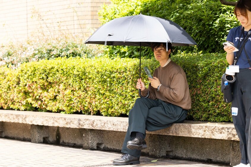 撮影当日は日差しが強く、日傘を持ってひと休みする松下さん。撮影を見学するギャラリーに笑顔で手を振り、応える場面もあった(撮影:写真映像部・上田泰世)