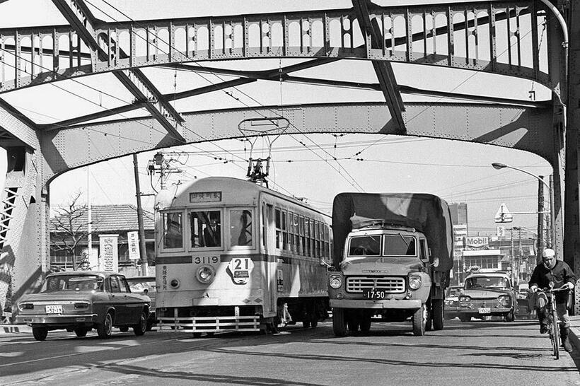 21系統も単独運行距離の長い路線だった。大型トラックから自転車まで、すさまじい雑踏の千住大橋を渡る御徒町駅前行きの都電。橋上を並走するのは1959年式のいすゞTXGトラック。千住仲組～千住大橋　（撮影／諸河久：1968年2月23日）