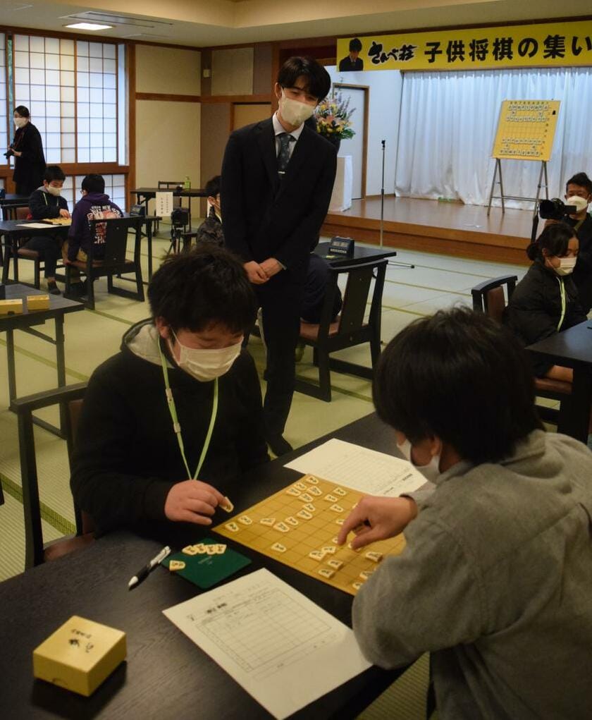 少し距離をとって子どもたちの対局を見つめる藤井聡太竜王。ブームを巻き起こした本人は、いたって冷静だ／3月12日、島根県で