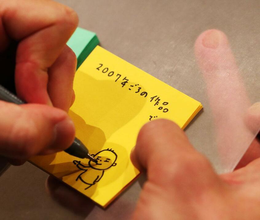 作品には、自筆で「付箋説明文」が付けられたものも。「こうやって、茶々を入れているんです」とヨシタケ。極細ペンで描かれたイラストは、指で隠れるほど小さく、絵本も原画を拡大してつくるという（撮影／写真映像部・加藤夏子）