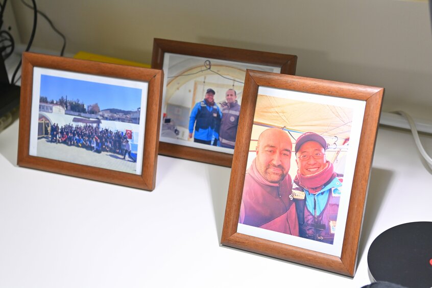 職場のデスクには、被災地で共に活動したチームの集合写真や、地元の医師と撮影した写真が並ぶ。写真=東川哲也(写真映像部)