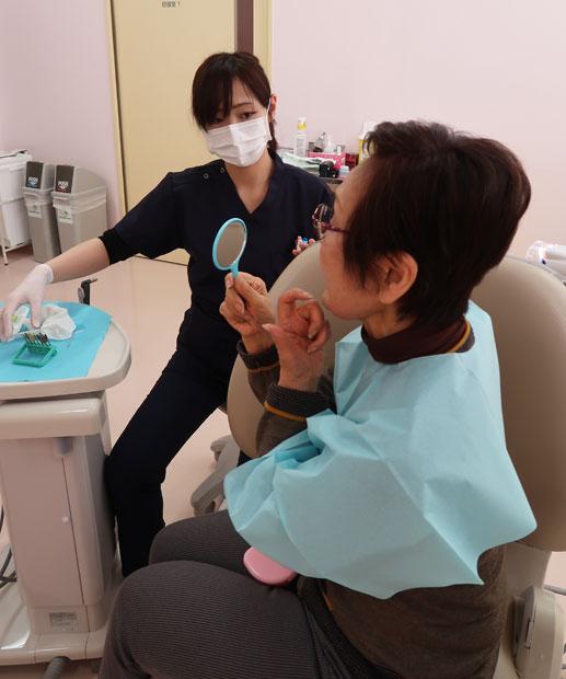 手鏡で口の内の様子を観察する女性患者。奥は歯科医師（多摩クリニック）