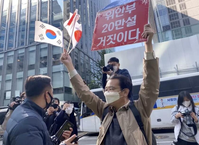 「慰安婦20 万人説は嘘」のプラカードを日韓の国旗を手にして掲げる男性（提供）