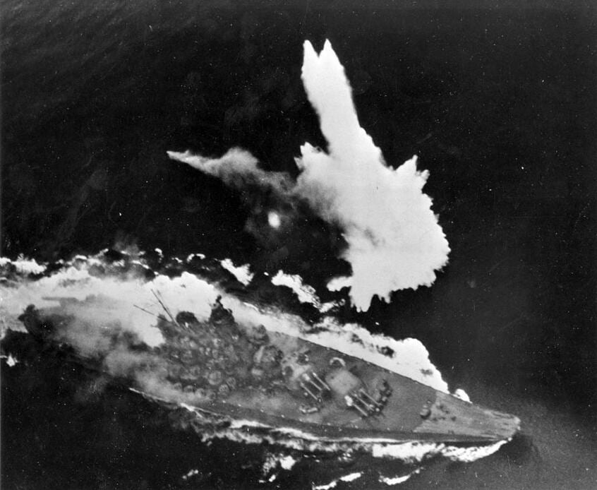 1945年4月7日、鹿児島沖の東シナ海で米空母艦載機の爆撃を避けようと、必死に操艦する大和。後部では火災が発生している。投下された爆弾が左舷の海上でさく裂し、巨大な水柱が立ち上がっている。同日、大和は3000人人以上の乗員とともに沈没した(米海軍歴史センター提供)