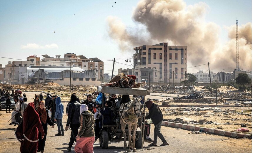 1月30日、パレスチナ人がガザ地区南部から逃げる中、背景に砲撃の煙が立ち込める（写真＝AFP/アフロ）