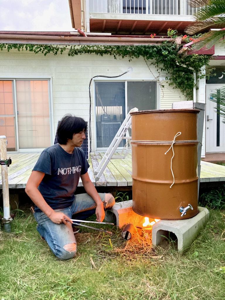 薪を燃やしてドラム缶風呂を沸かす高坂さん。右後ろ側の排気口に網をのせて野菜などを焼き、雑談しながら約１時間かけて適温になるのを待つ（撮影／今村拓馬）