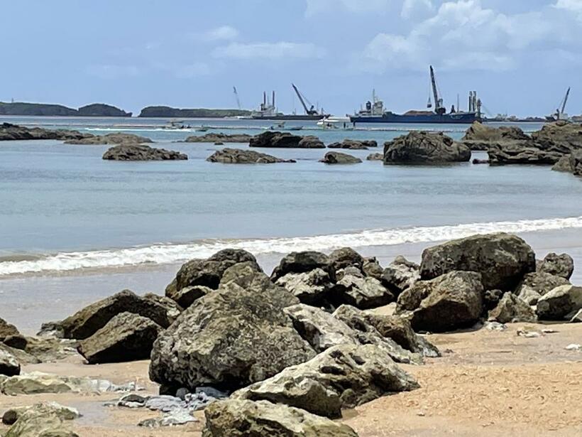 瀬嵩浜に打ち寄せる穏やかな波の向こうに、沖縄県名護市辺野古で進む新基地建設が一望できる。多様な貝を育む大浦湾の海底も埋め立てが予定されている（ｐｈｏｔｏ　編集部・渡辺　豪）