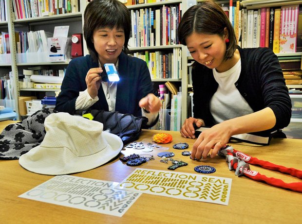 シールをデザインした神戸芸術工科大学の実習助手、宮谷さん（右）とプロジェクトの学内研究代表者、吉田准教授。帽子やアクセサリーなど生活に取り入れやすい反射材グッズを提案する