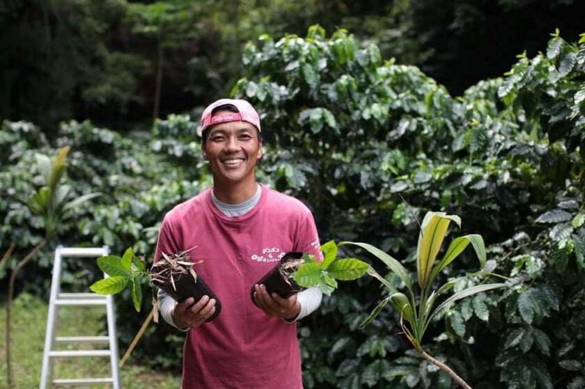 徳之島でコーヒー農園を営む宮出博史さん。手にしているのはコーヒーの苗木（写真：宮出さん提供）