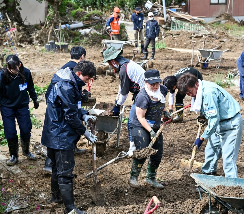 高齢女性の自宅の畑に流れ込んだ土砂をかき出すボランティアたち=2024年10月20日、石川県輪島市町野町