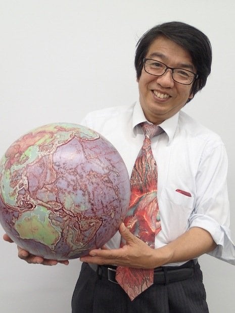 赤色立体地図の地球儀と千葉さん。ネクタイはは赤色立体地図をプリントしたもの。グッドデザイン賞も受賞したこの地図はアートとしても優秀？！