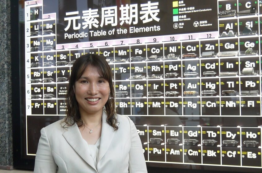 物質・材料研究機構の玄関にある元素周期表の前に立つ桂ゆかりさん